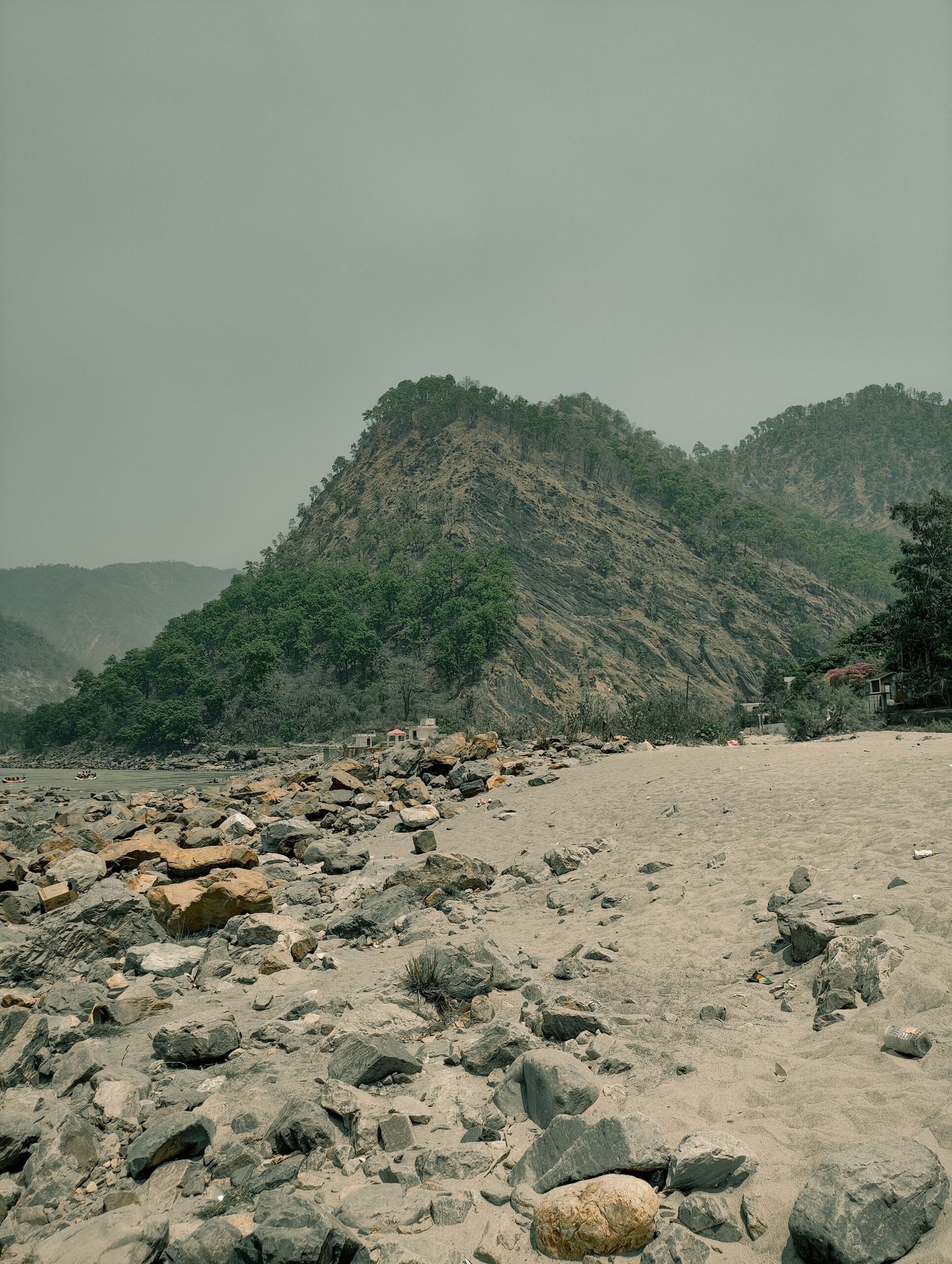 Lush green hills by a rocky beach in Rishikesh, India offer a serene natural landscape.