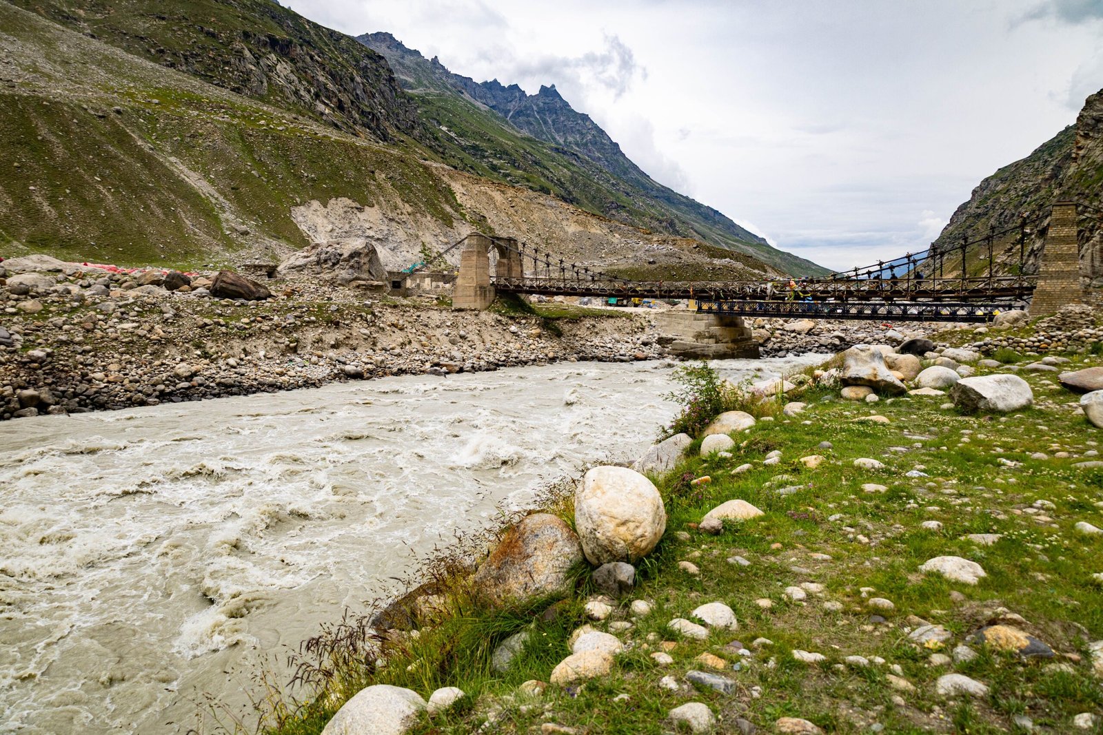 Picturesque view of a rocky river and suspension bridge amidst the Himalayan mountains.